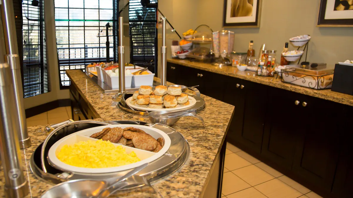 This interior image features a well-lit breakfast area with a granite countertop displaying a variety of breakfast food items and serving utensils, set beside a window streaming in natural light. The inviting scene suggests a communal space perfect for starting the day and socializing over a meal.