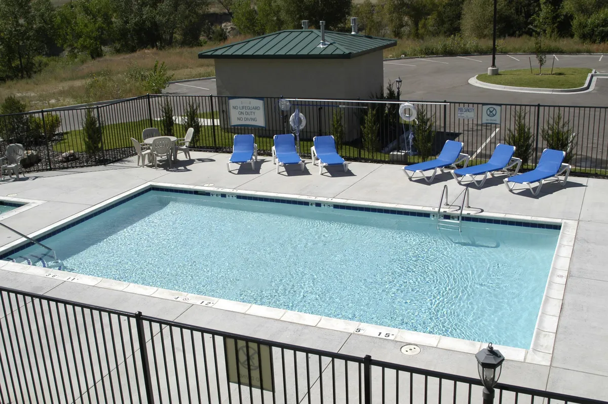 This image captures a tranquil outdoor swimming pool surrounded by lush greenery and lounge chairs, set against a scenic backdrop. The area is inviting for both relaxation and recreation, with clear blue water perfect for a summer dip. The surrounding landscape hints at nearby mountains, reinforcing the property's connection to the outdoors and adventure.