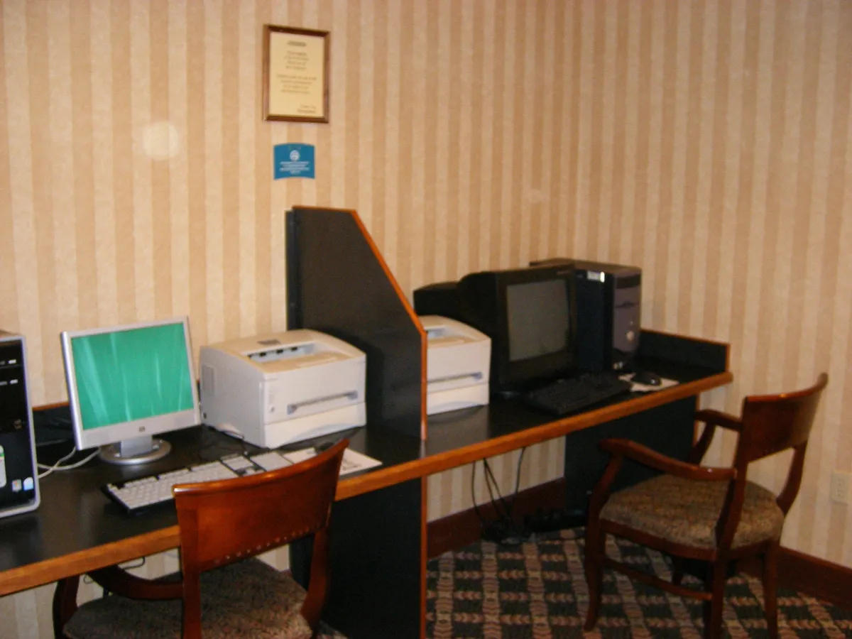 An interior view of the business center, featuring several computers, printers, and ergonomic chairs. The space is well-lit and designed for productivity, signaling an environment where business travelers can comfortably work or host meetings during their stay.